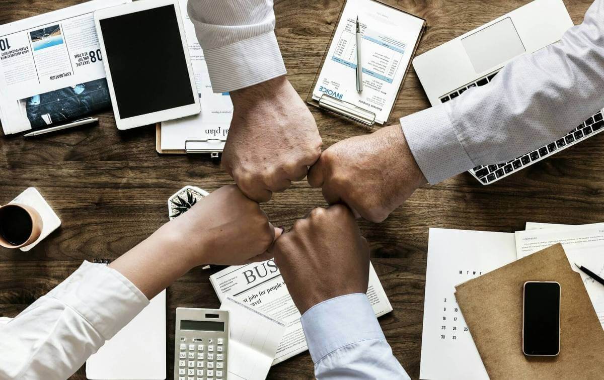 An overhead picture of a desk with four arms fist-bumping in the middle of it. The fist bump symbolizes culture.