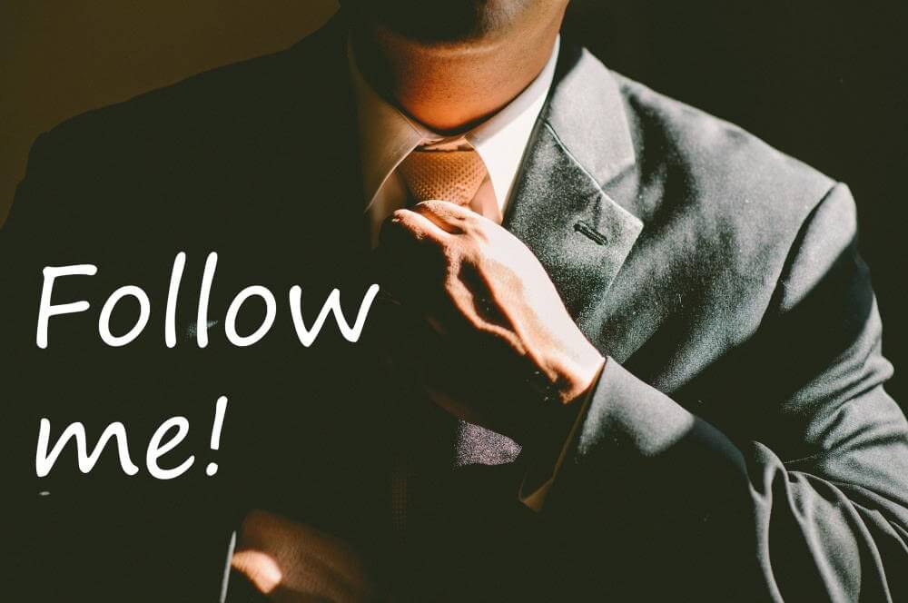 Encourage Leadership: A picture of a man wearing a gray suit with a white collared shirt and orange tie. He is visible from his mid-chest up to his chin. His hands are straightening his tie and jacket. The words "Follow me" show in the lower left of the picture.