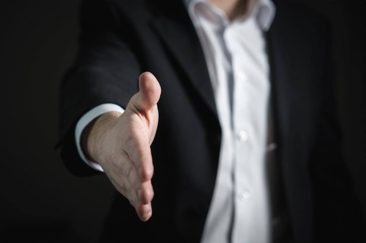 A picture of a man, visible from the neck to the waist. He's wearing a black suit jacket and white button-down shirt. His hand is extended toward the camera, reaching for a handshake. This is meant to symbolize keeping your focus on sales.