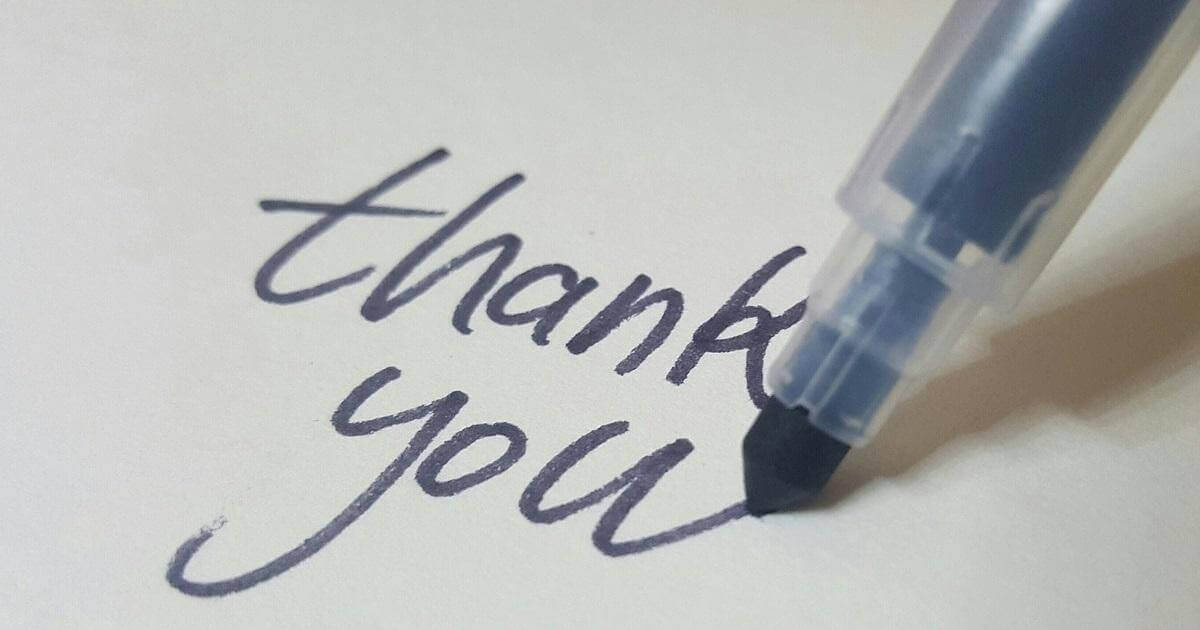 Picture of the words "thank you" written by hand on a piece of paper. The pen is still visible in the picture and has just completed the "u" in the word "you".