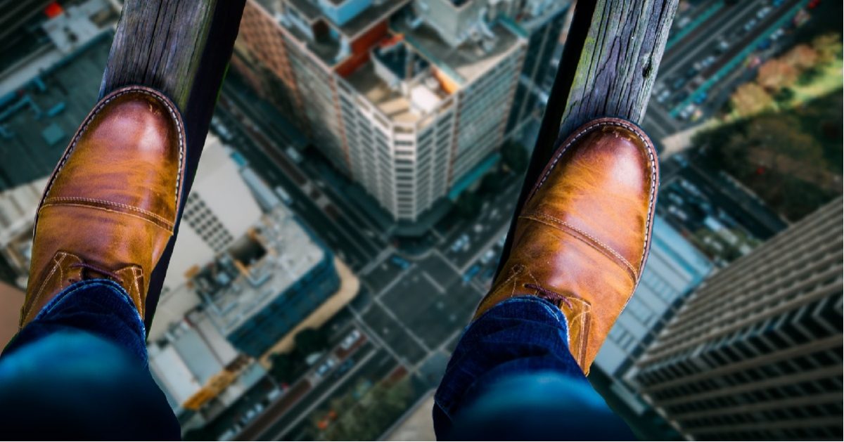Symbolic image for fear of failure. Shows two narrow boards stretching high above a city. Viewpoint is from person balanced on those boards, looking down at their shoes, standing on the boards, with the cityscape far below.