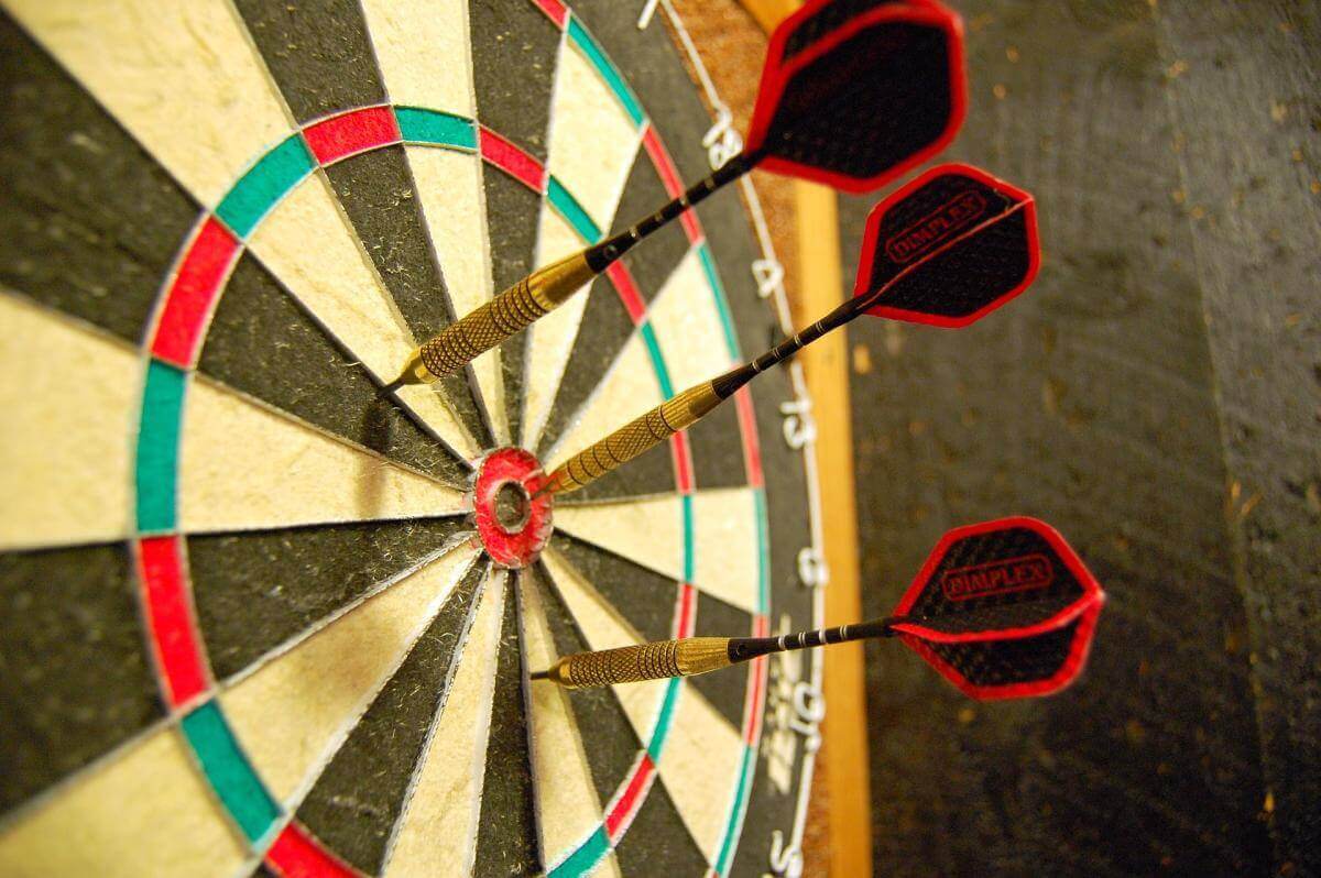 A picture of a dartboard with three darts sticking out of it. One is in the bulls-eye, the other two are a little bit outside the bulls-eye.